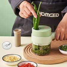 Person using a green electric vegetable chopper to slice peppers, demonstrating its 4-in-1 multifunction capability.